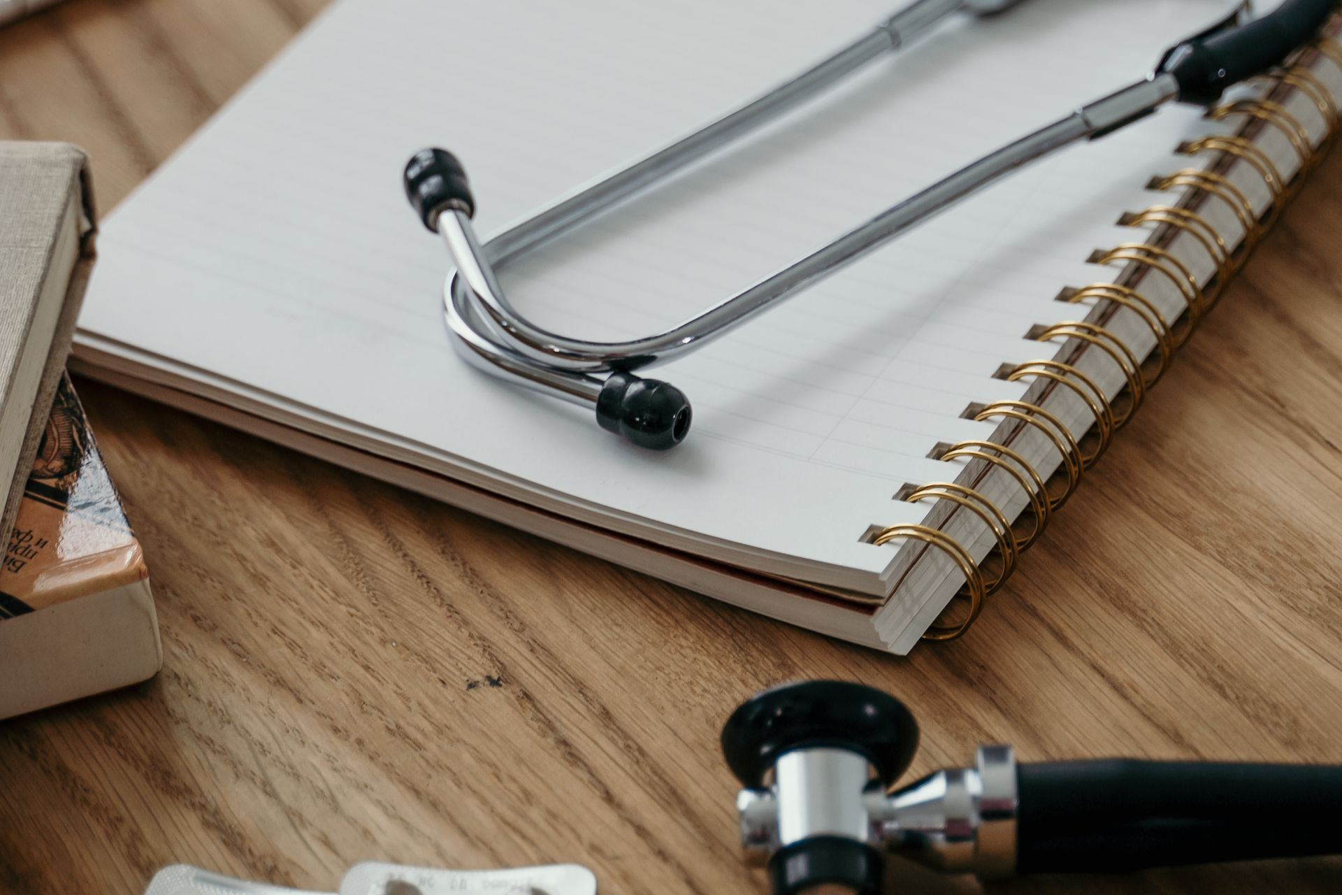 Duas pessoas do setor de autorização de um hospital diante de um monitor, com a guia de solicitação aberta na tela, uma pilha de pedidos médicos e laudos sobre a mesa e um telefone fora do gancho.