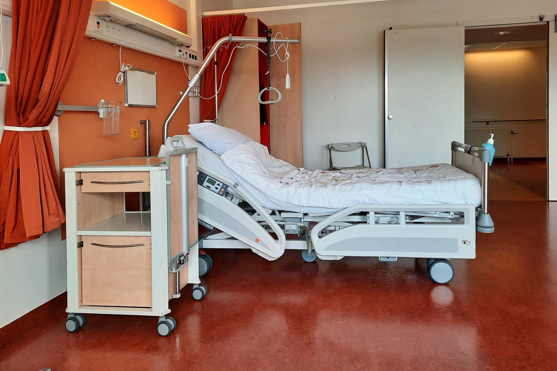 Enfermeira de pé no posto de enfermagem de uma unidade de internação, à noite, com o painel de leitos ao lado e uma prancheta na mão, conferindo os pacientes cuja autorização vence no dia seguinte.