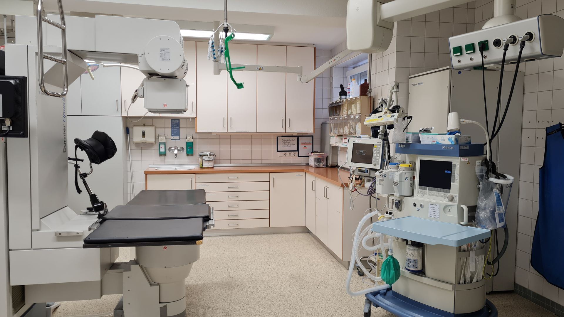 Analista de autorização em uma sala administrativa de hospital, com dois monitores abertos na consulta do rol da ANS e um pedido de procedimento impresso sobre a mesa.