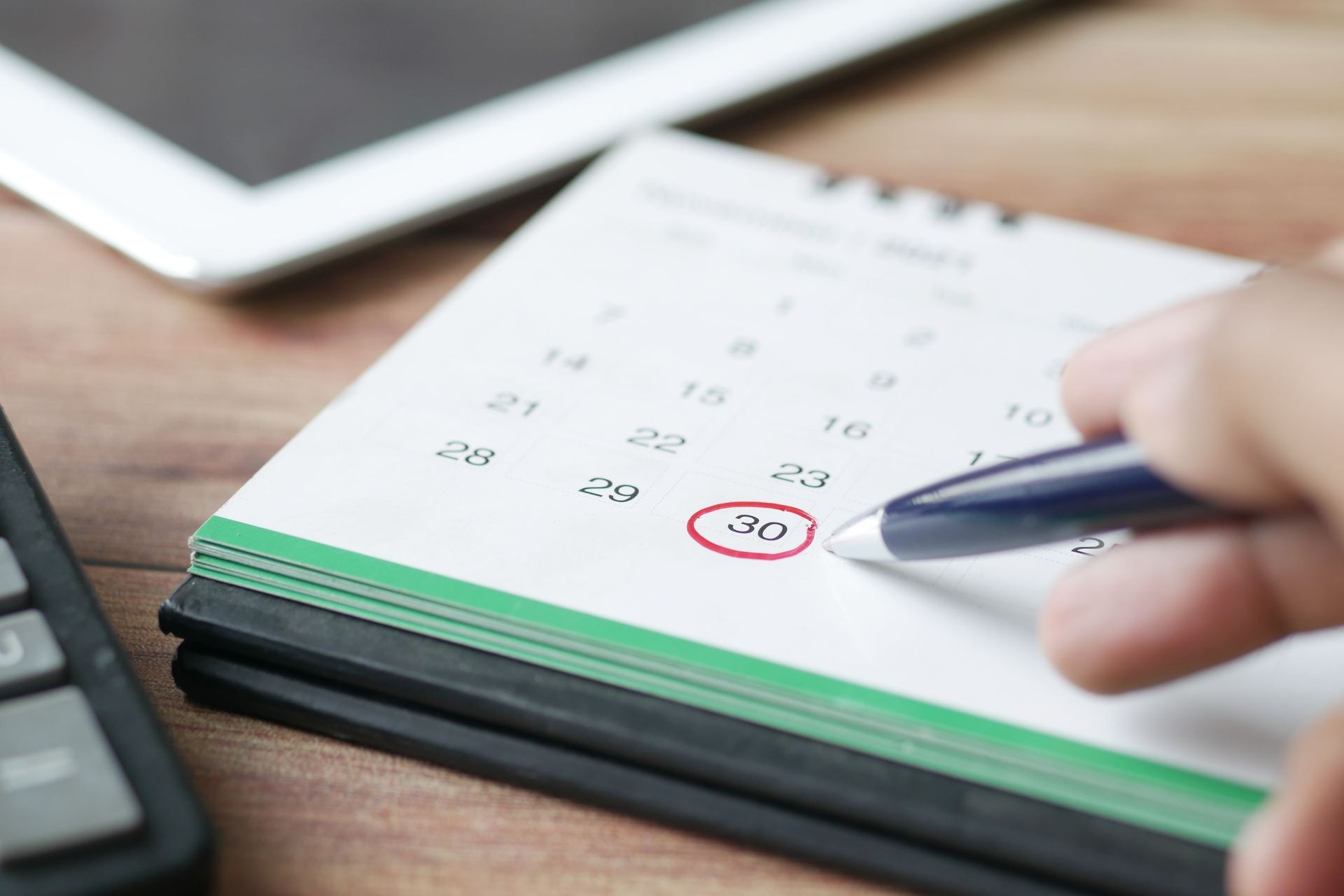 Mão marcando uma data em um calendário de mesa ao lado de uma calculadora